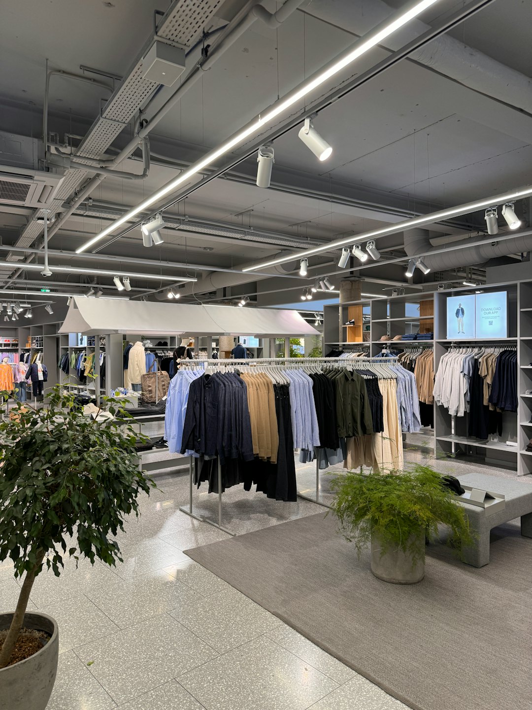 Negozio di abbigliamento moderno con scaffali di vestiti e schermo promozionale.