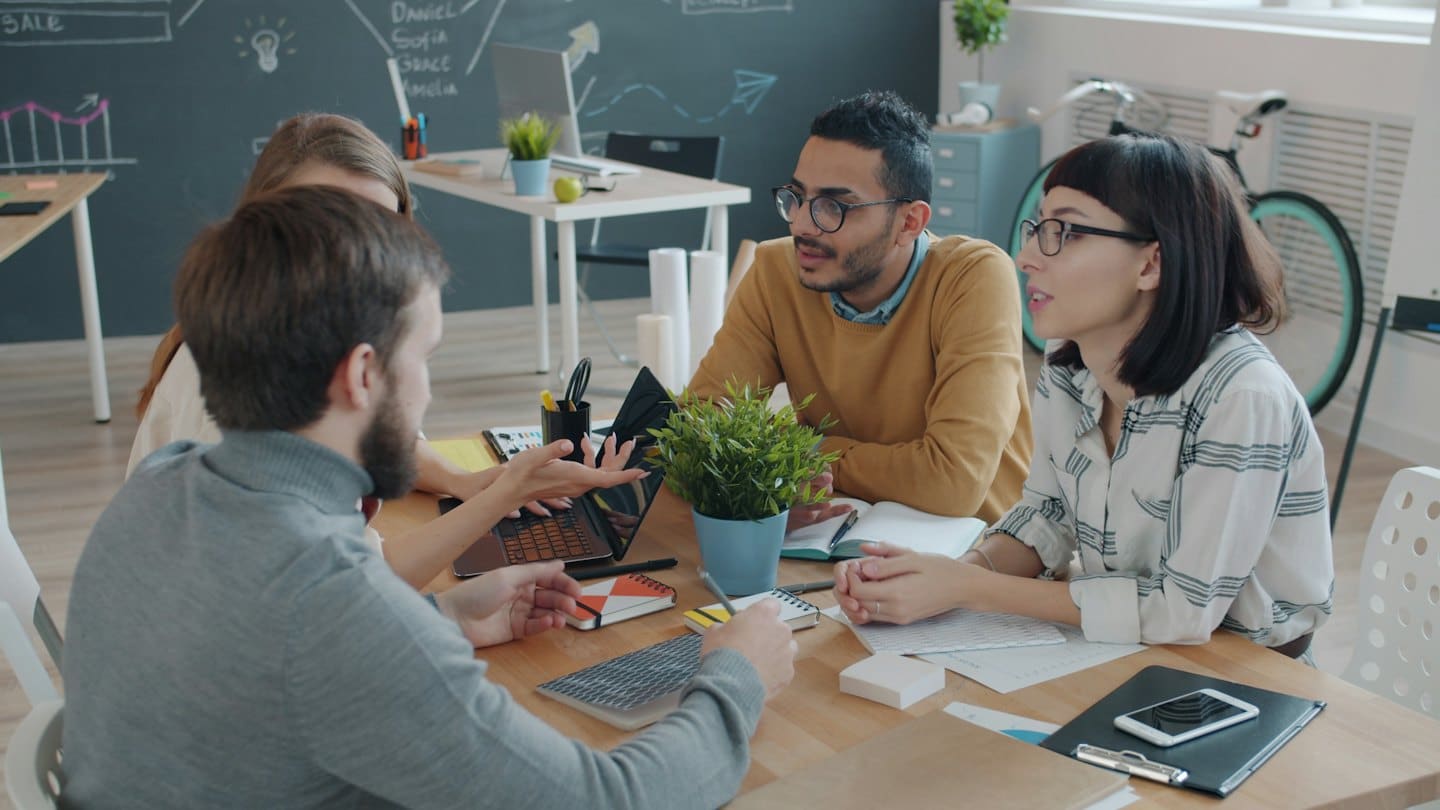Professionisti diversi collaborano attorno a un tavolo con laptop e appunti.